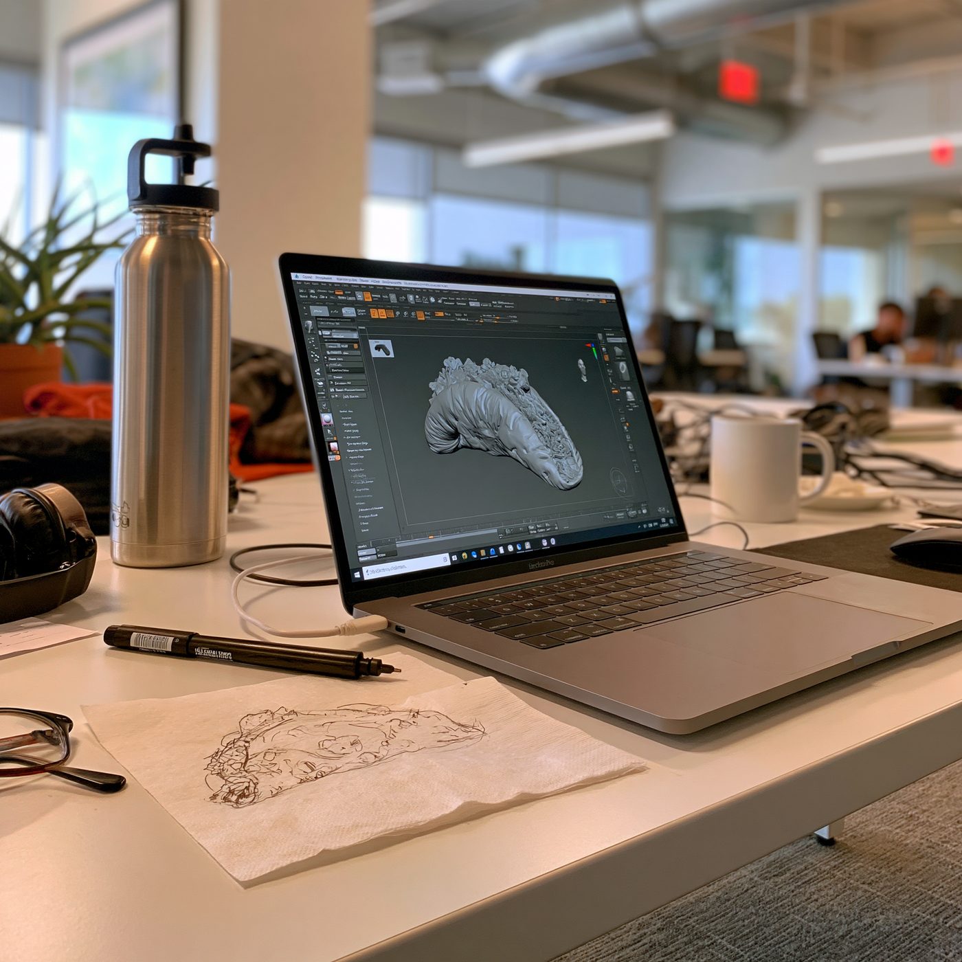 A pen sketch on a napkin next to a laptop showing the 3D model of the same shape